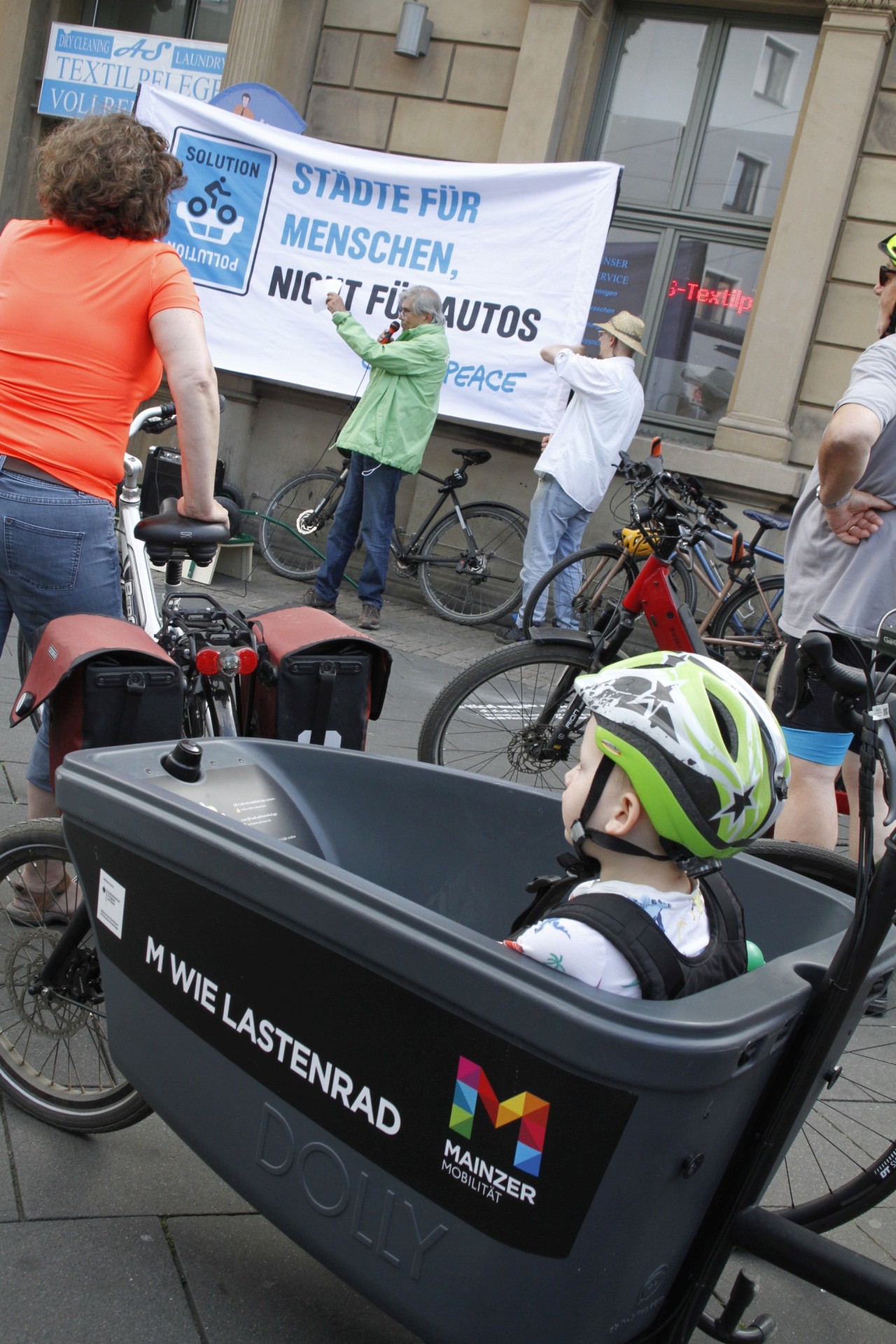 Raddemo-Junge-Lastenrad_IMG_1280 Auftaktkundgebung vor dem Mainzer Hauptbahnhof mit Oleg Cernavin (grüne Jacke vor dem Transparent), im Vordergrund ein kleiner Teilnehmer im Lastenrad seines Vaters.